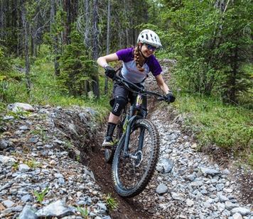 Young girl smiling as she rides down a mountain bike trail through the forest.