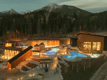 An aerial view of Everwild spa at dusk, featuring several pools and sauna buildings with a mountain in the background.