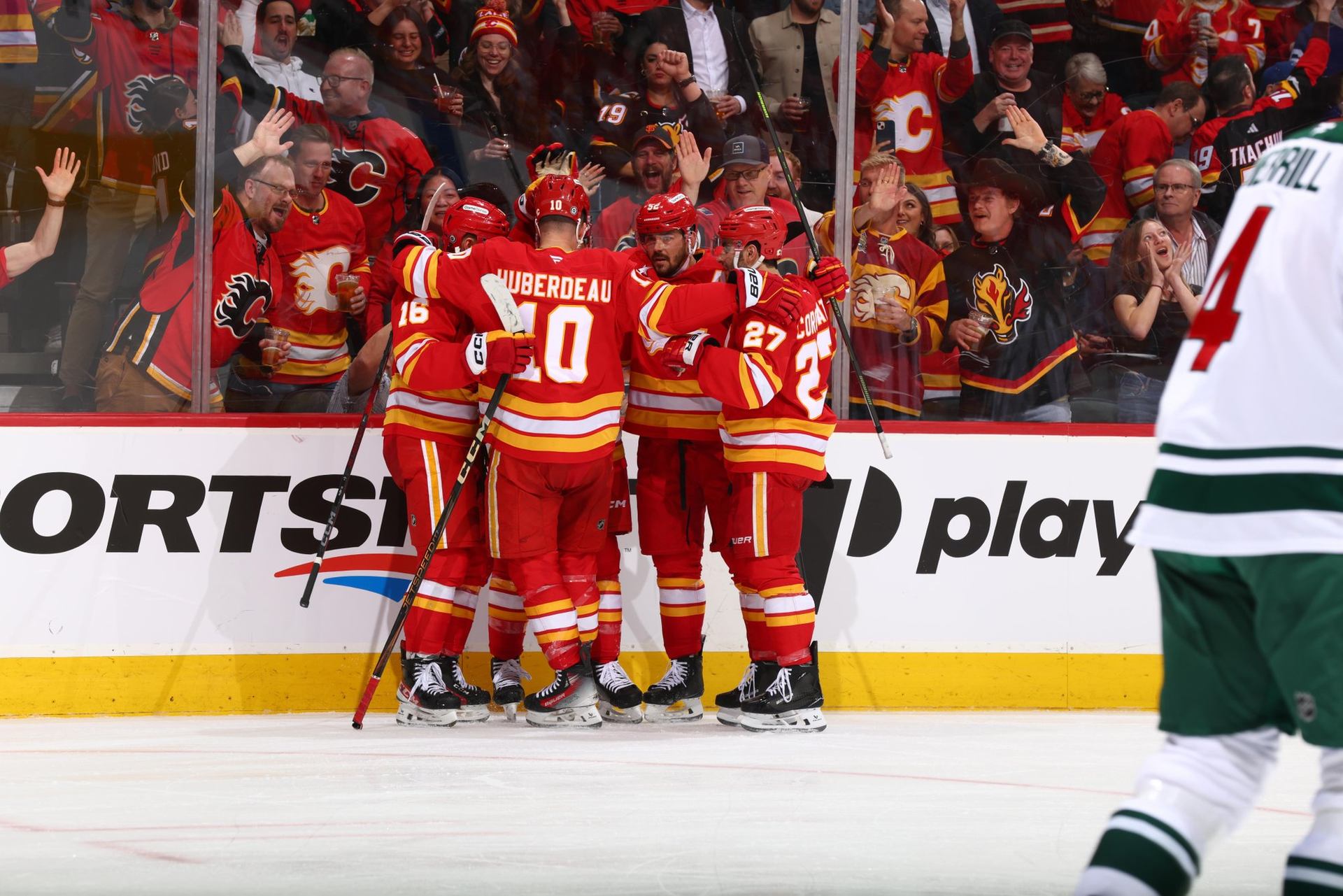 Calgary Flames hockey players cheer on the ice with an excited crowd in the stands behind them.