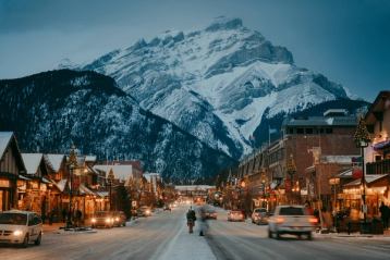 An idyllic winter moment on Banff Avenue at dusk, with shops lining either side of a street that seems to lead toward a mountain.