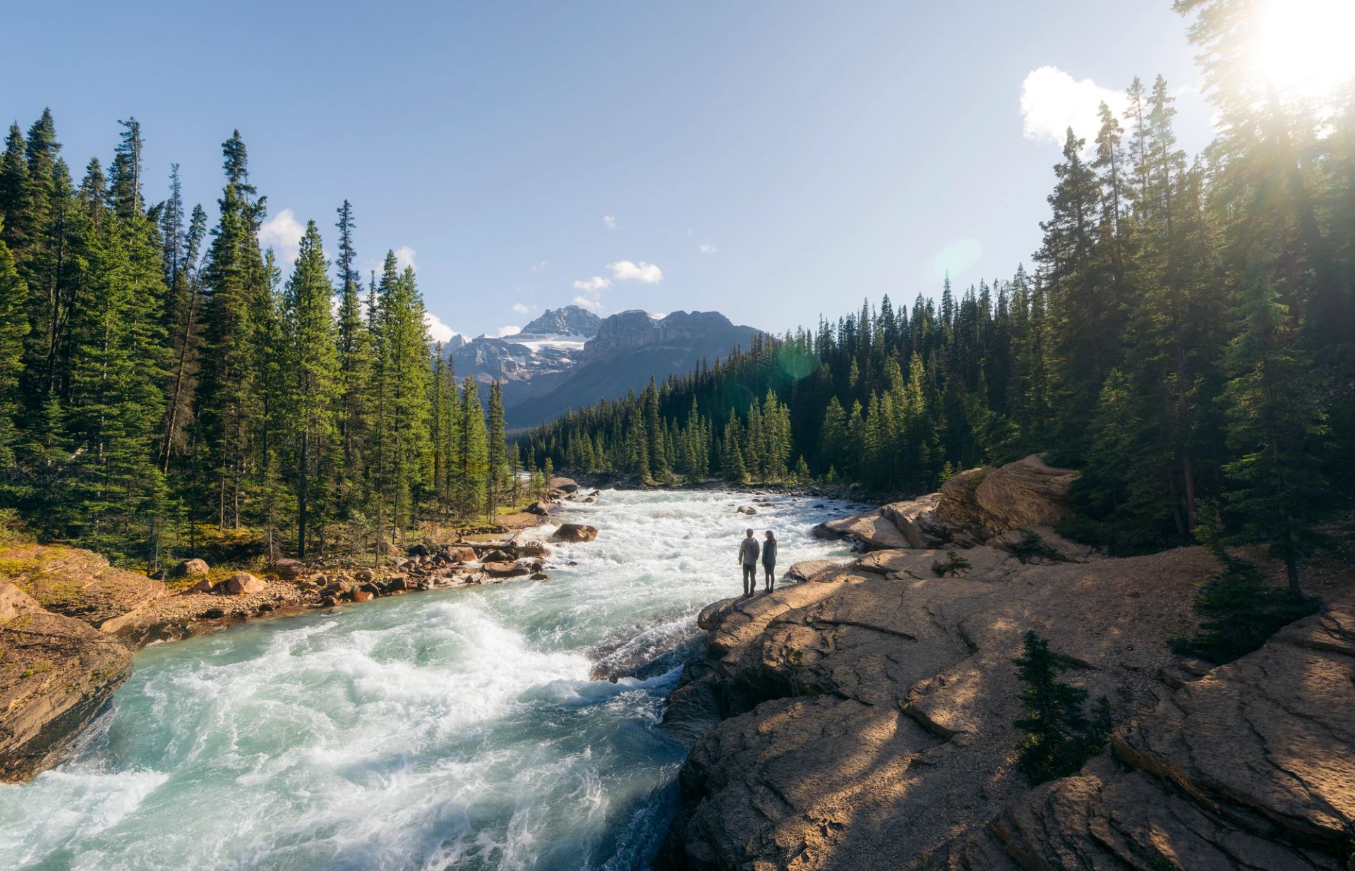 Two people stand atop a rock that overlooks Mistaya Canyon.