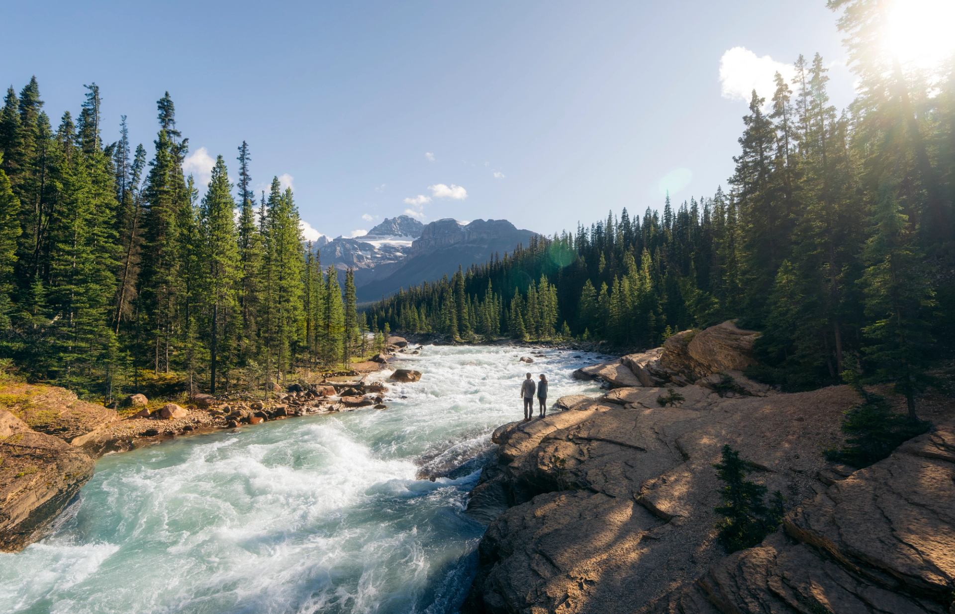 Two people stand atop a rock that overlooks Mistaya Canyon.