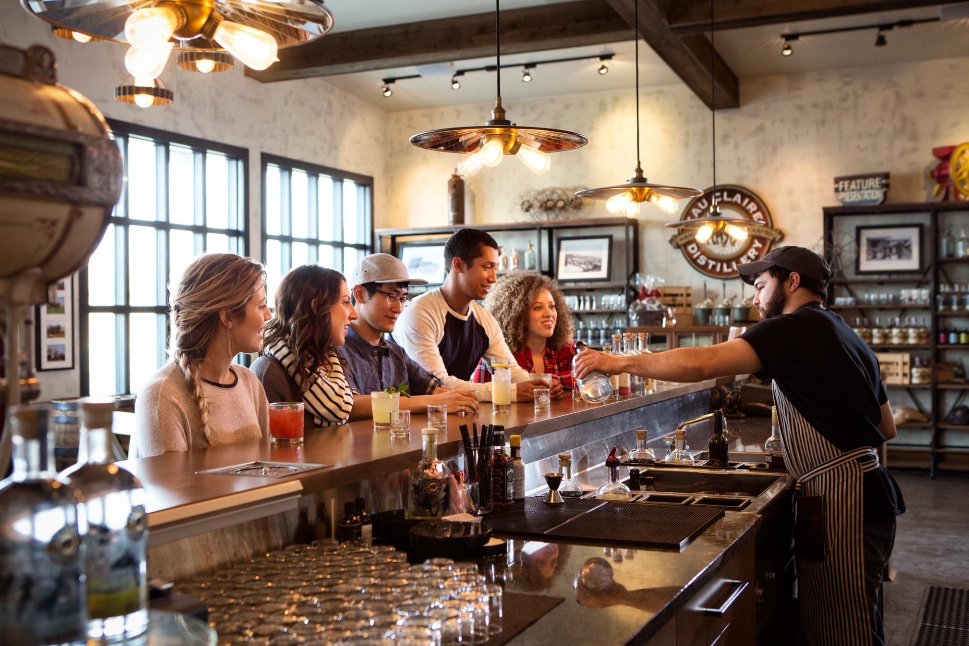 A group of friends watching a bartender pour during a tasting at a Distillery