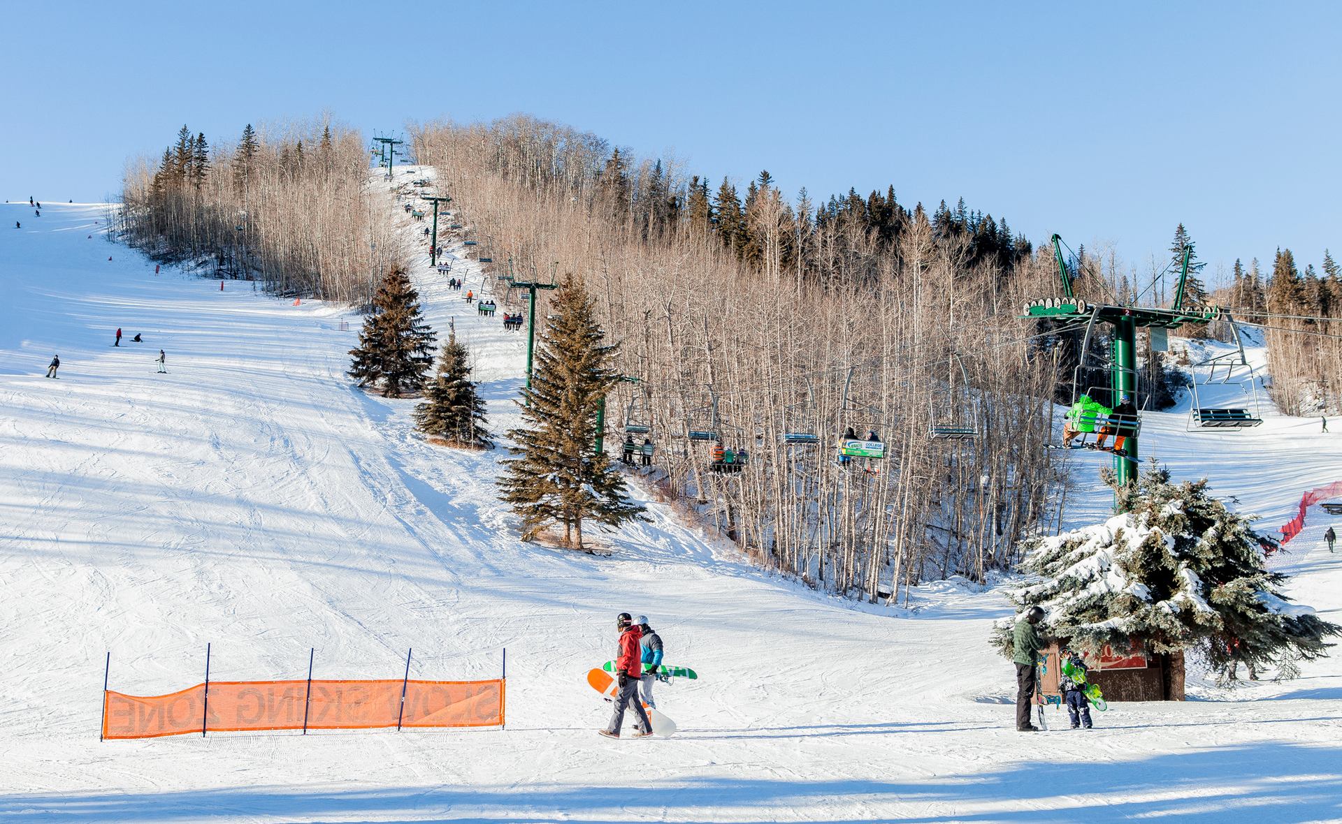 Skiers and snowboarders on a ski  hill with a chairlift overhead.