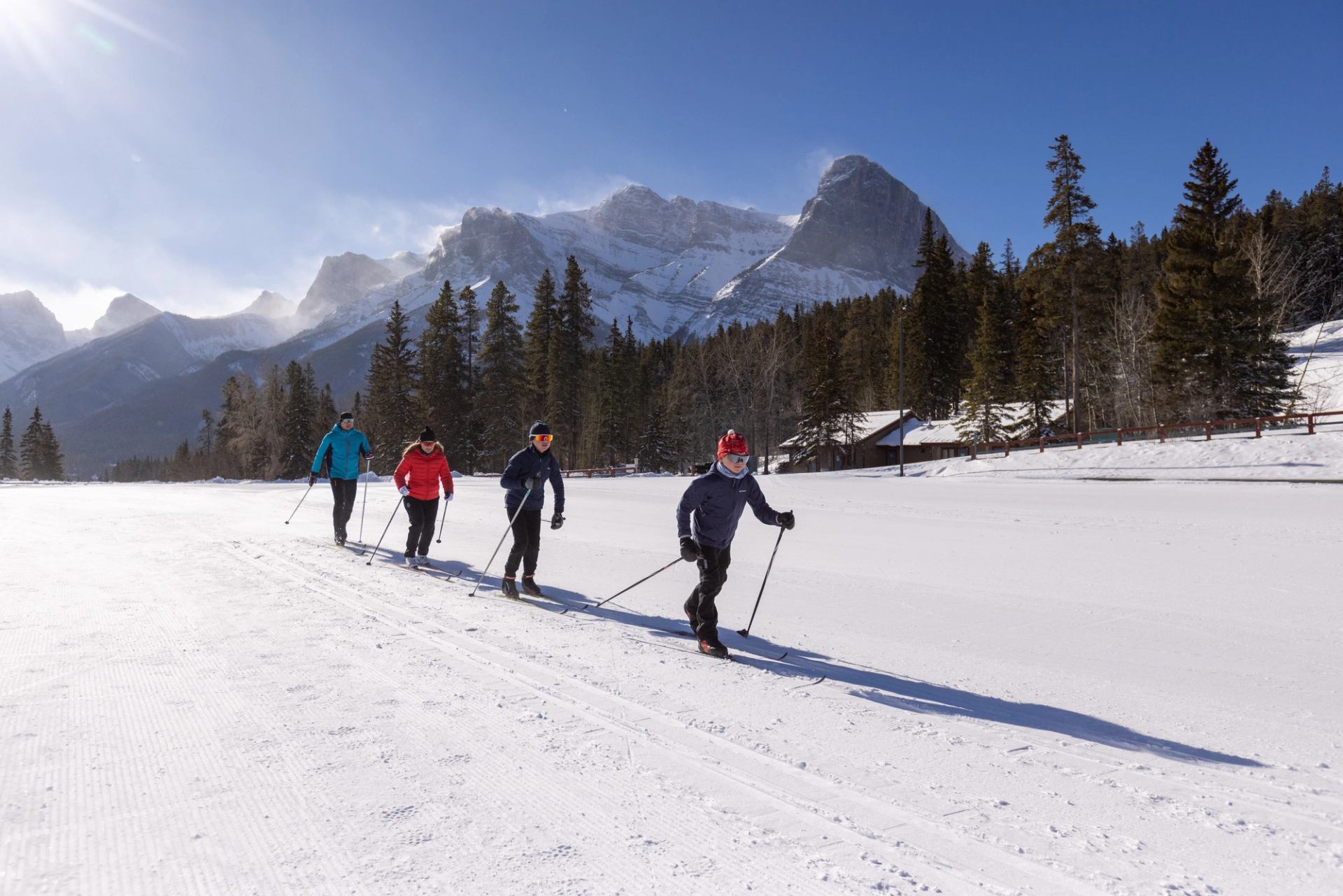 Family of four cross country skiing with mountains in the background.