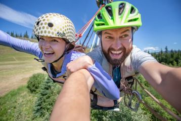 Close up on a man and woman smiling as they ride down a zipline.