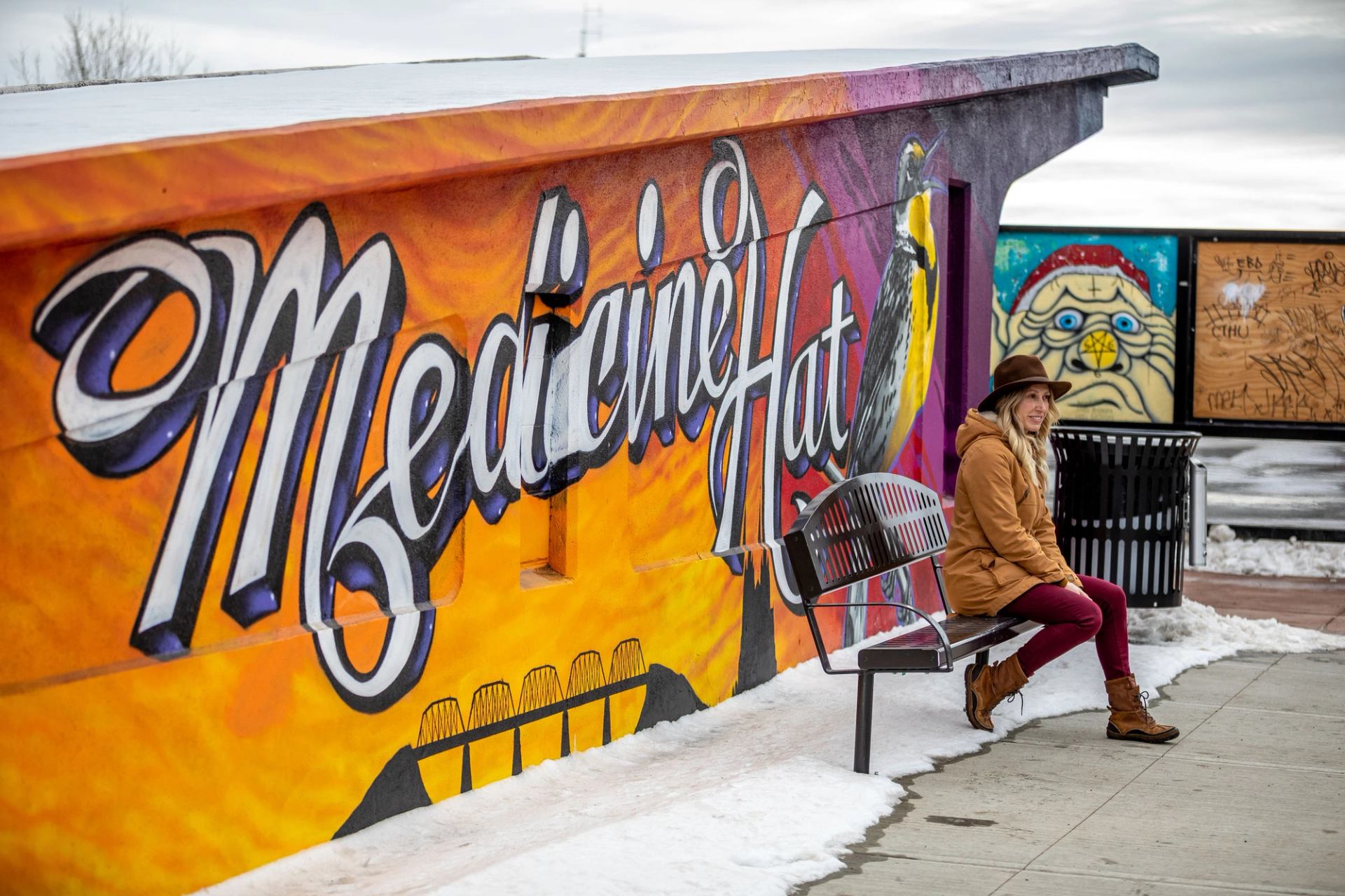 Woman sitting on a bench in front of a mural.