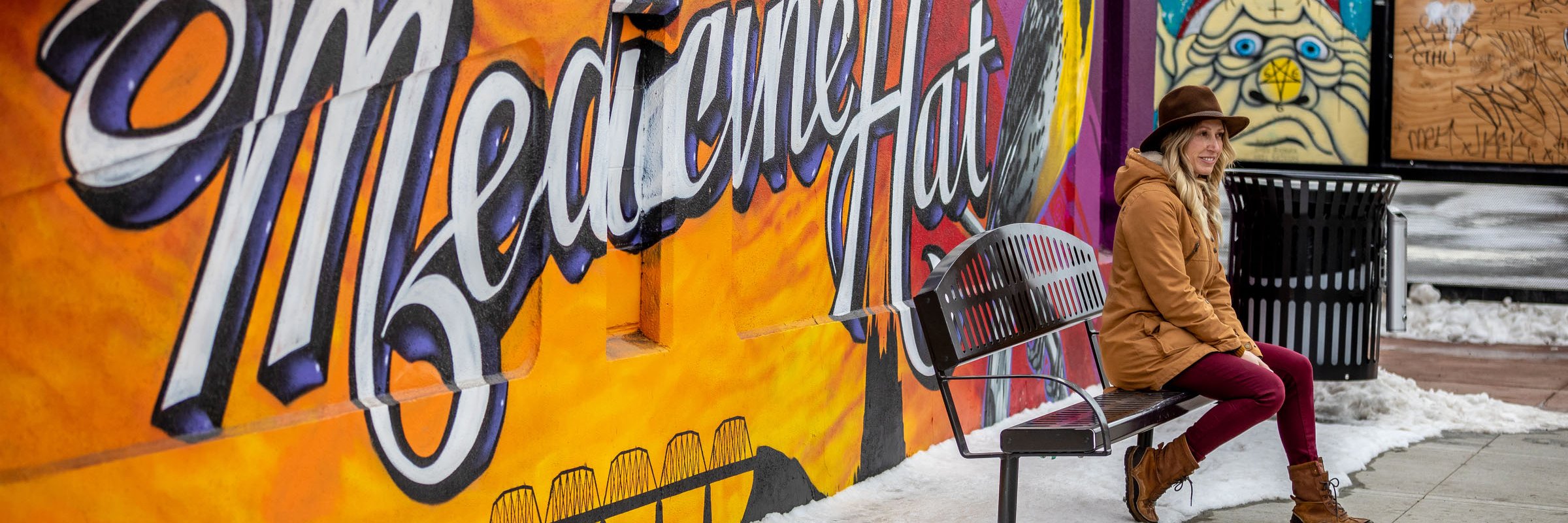 Woman sitting on a bench in front of a mural.