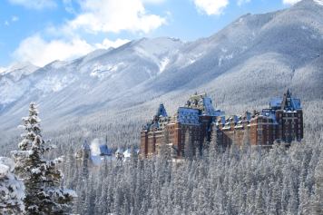 The Fairmont Banff Springs Hotel surrounded by snow-dusted pine trees and the Rocky Mountains.