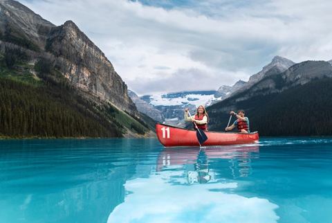 Young couple canoeing on Lake Louise on a sunny day. They are surrounded mountains. Making for a peaceful relaxing adventurous atmosphere.