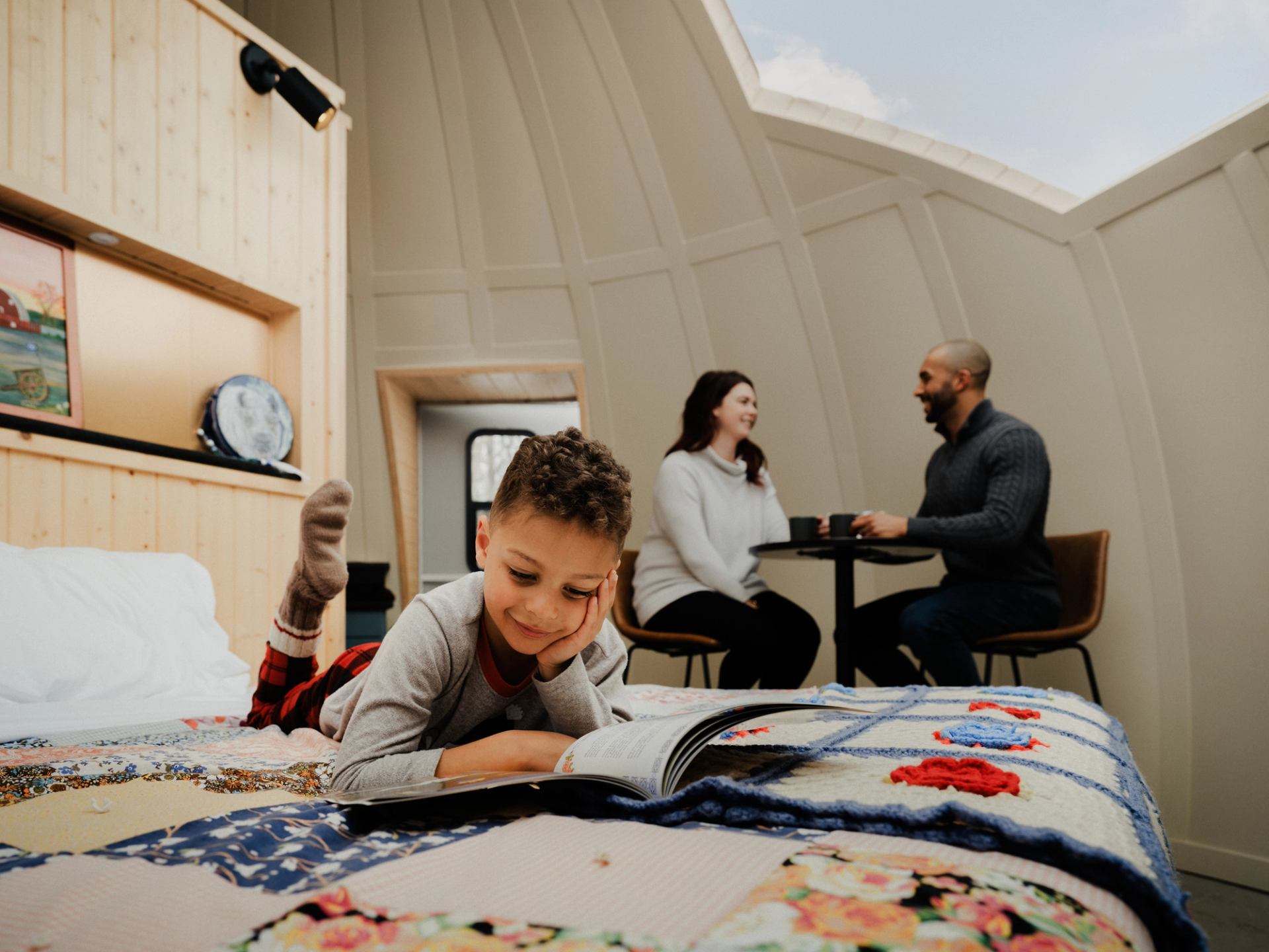 A child reads in bed in a sky-watching dome at Métis Crossing while his parents enjoy coffee.