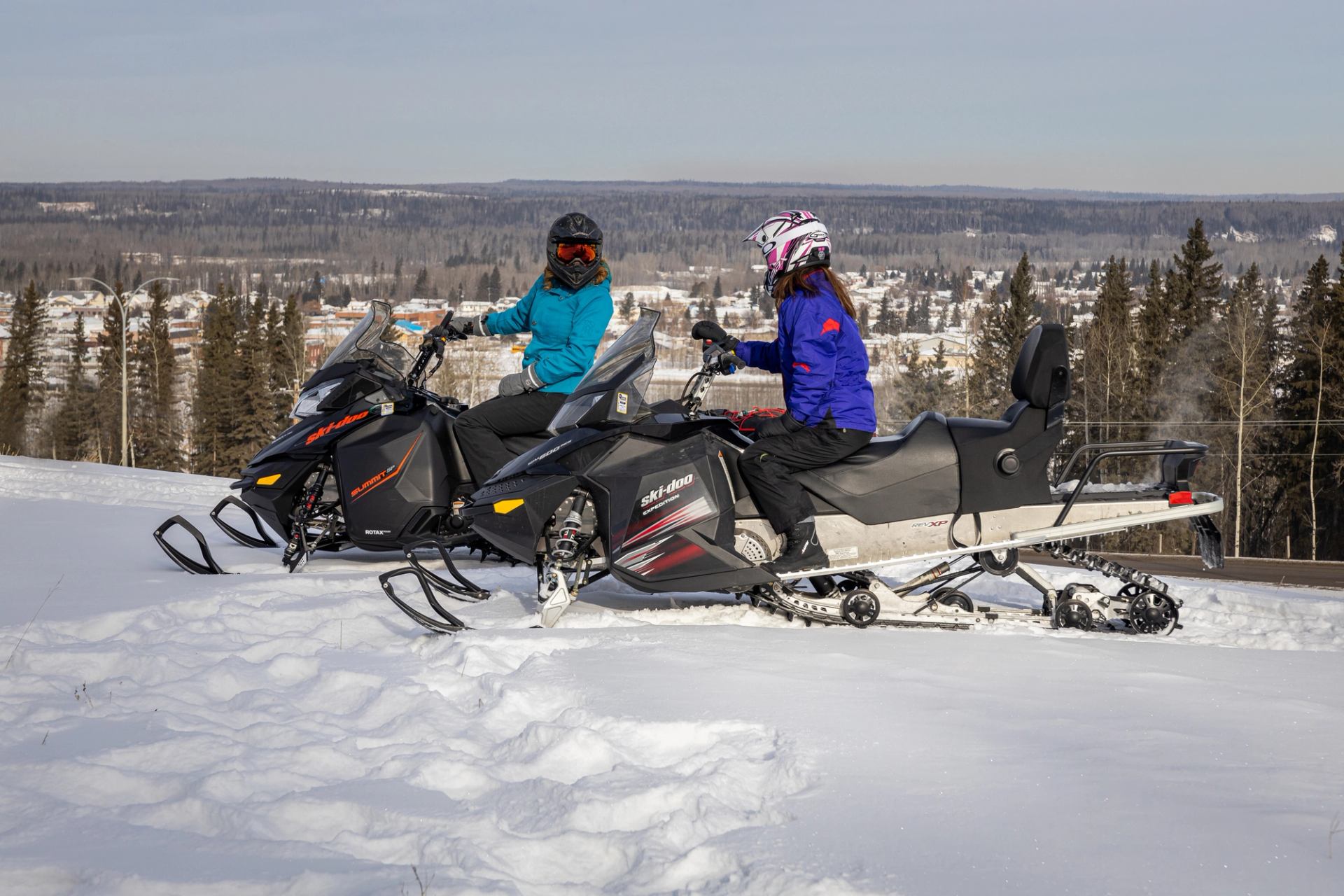 Two people on snowmobiles stop to chat before snowmobiling on a winter's day.