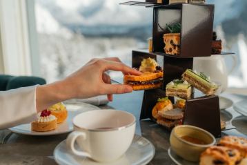 Hand reaching for pastries to go with their tea from a shelf of options.