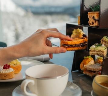 Hand reaching for pastries to go with their tea from a shelf of options.