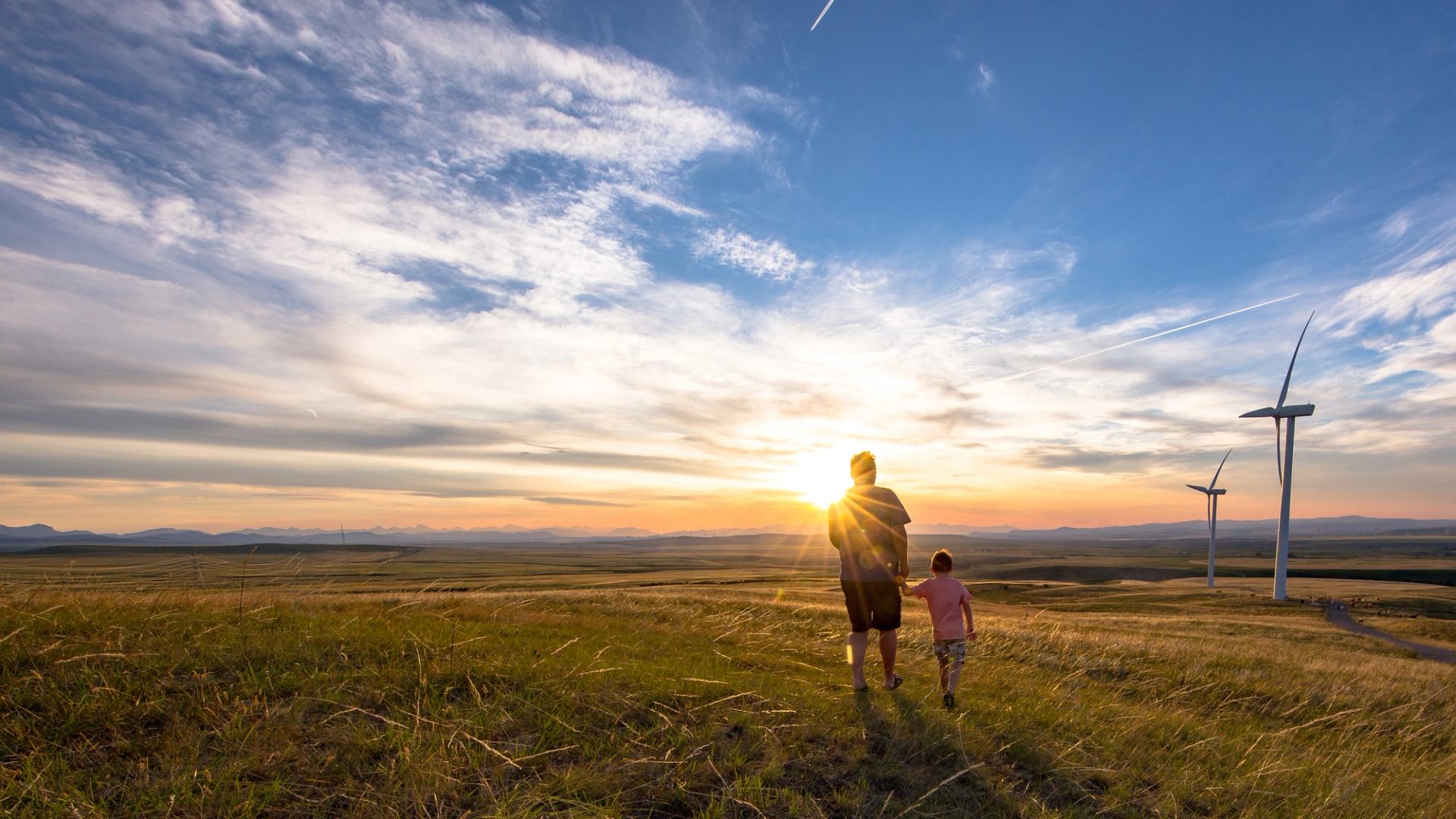 Family walking through a field with windmills at sunset in Oldman Dam Provincial Recreation Area near Pincher Creek.