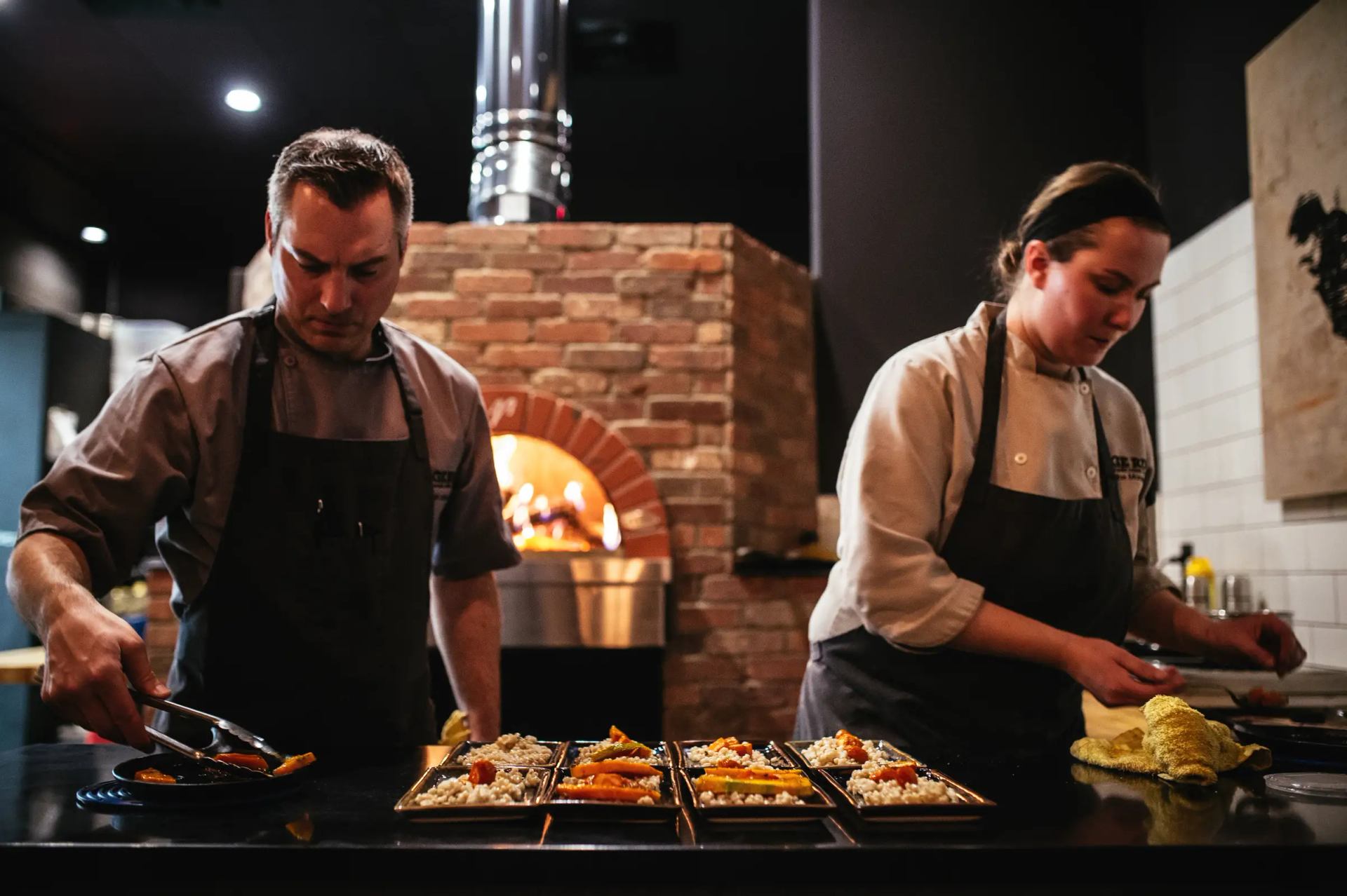 Chefs preparing plates of food in front of food burning fireplace