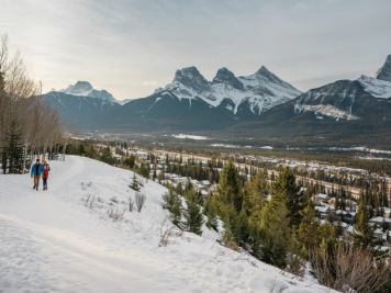 Couple walking along a trail in Canmore with the Three Sisters mountains in the background.