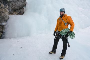 Man smiling in his ice climbing gear as he prepares for his climb from the bottom of a ice wall.