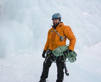 Man smiling in his ice climbing gear as he prepares for his climb from the bottom of a ice wall.