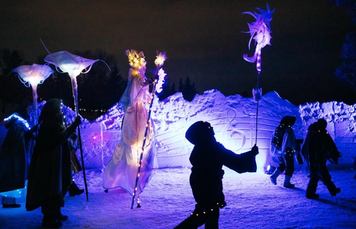 A group of performers walk down an icy path while holding light sticks at night.
