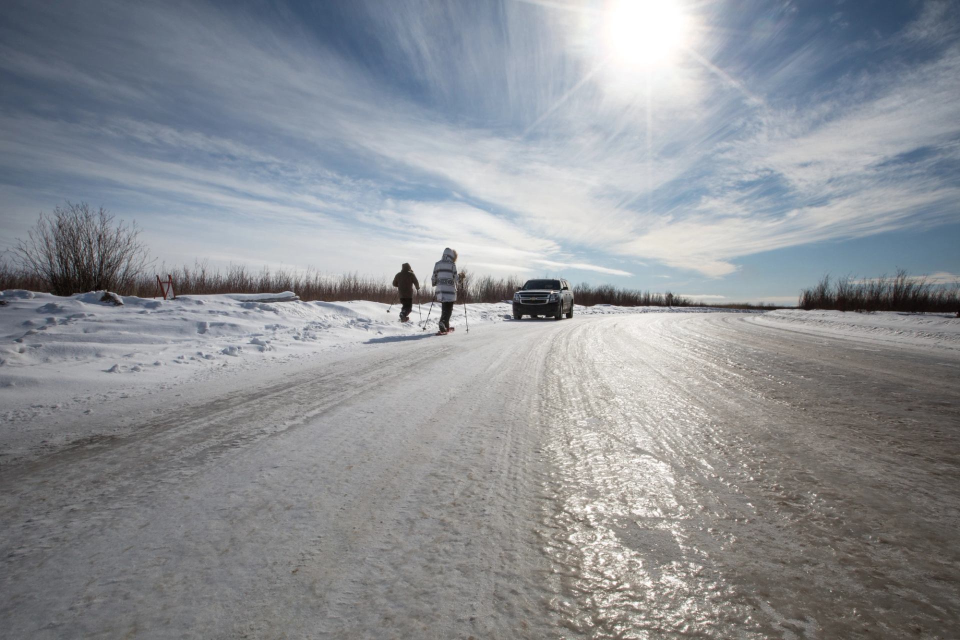 Two people and a car on a winter road to Fort Chipewyan from Fort McMurray.