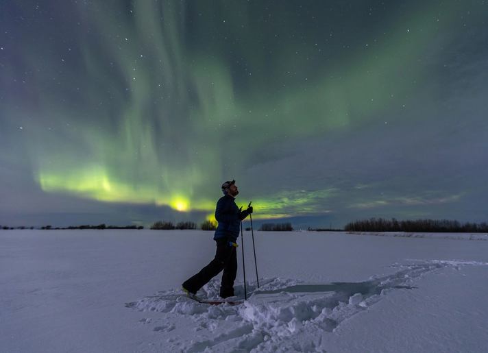 Cross country skier under a northern light sky.