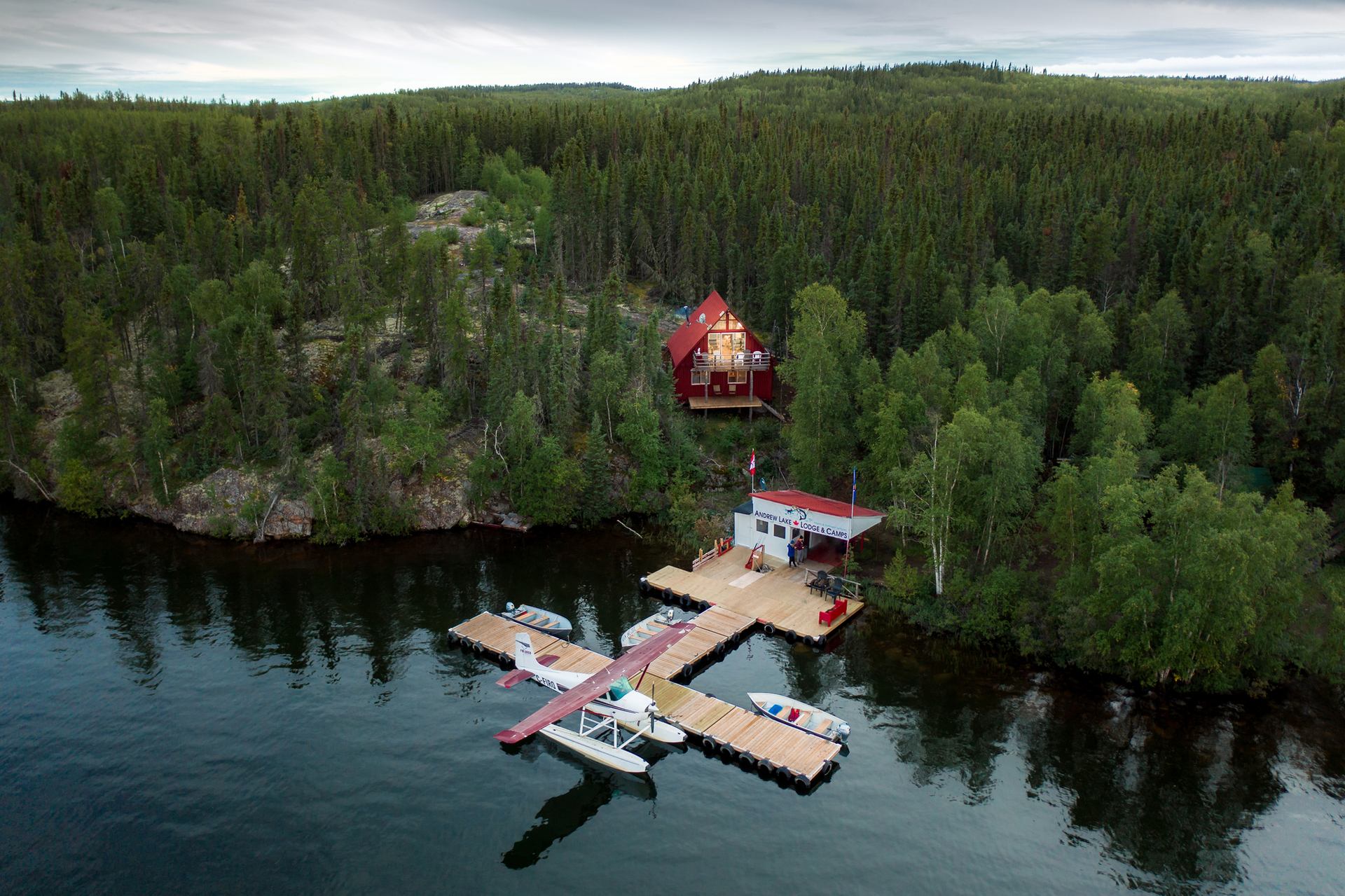 Aerial view of a lodge, dock and float plane on a lake surrounded by trees.