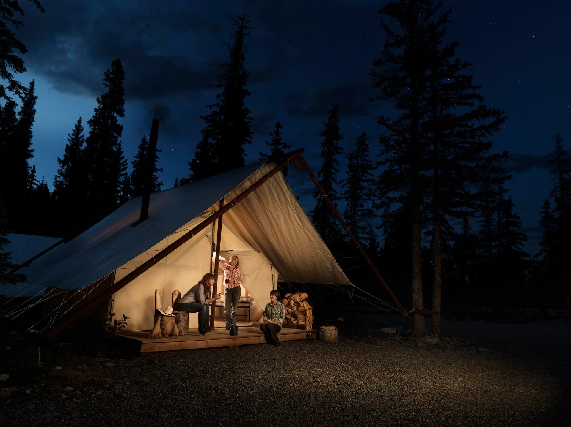 Three women drinking cocoa outside a tent while glamping luxury camping in Sundre in Central Alberta.