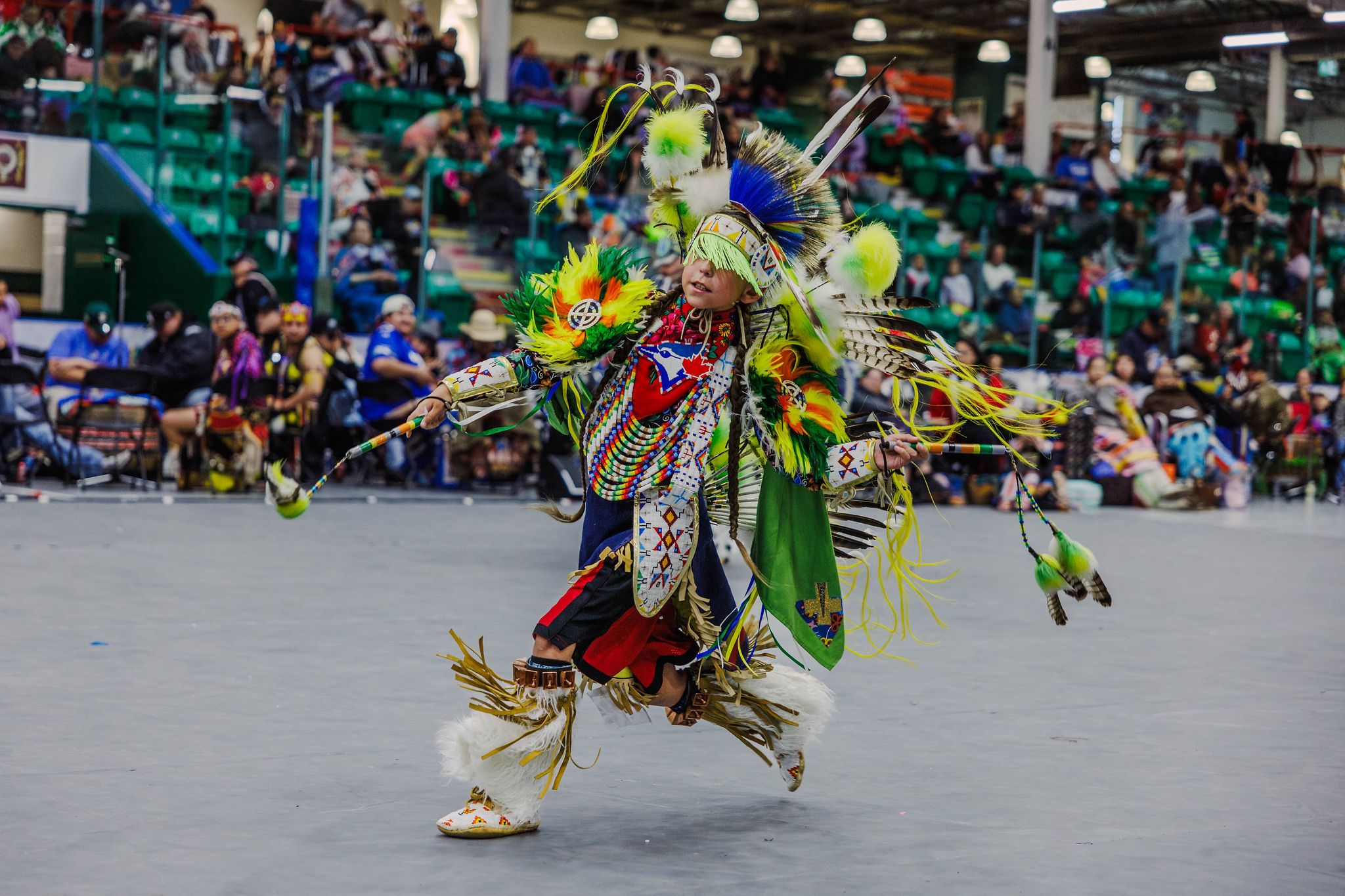 A young powwow dancer in colourful regalia, featuring lime green, bright yellow and other colours, performs at a powwow.