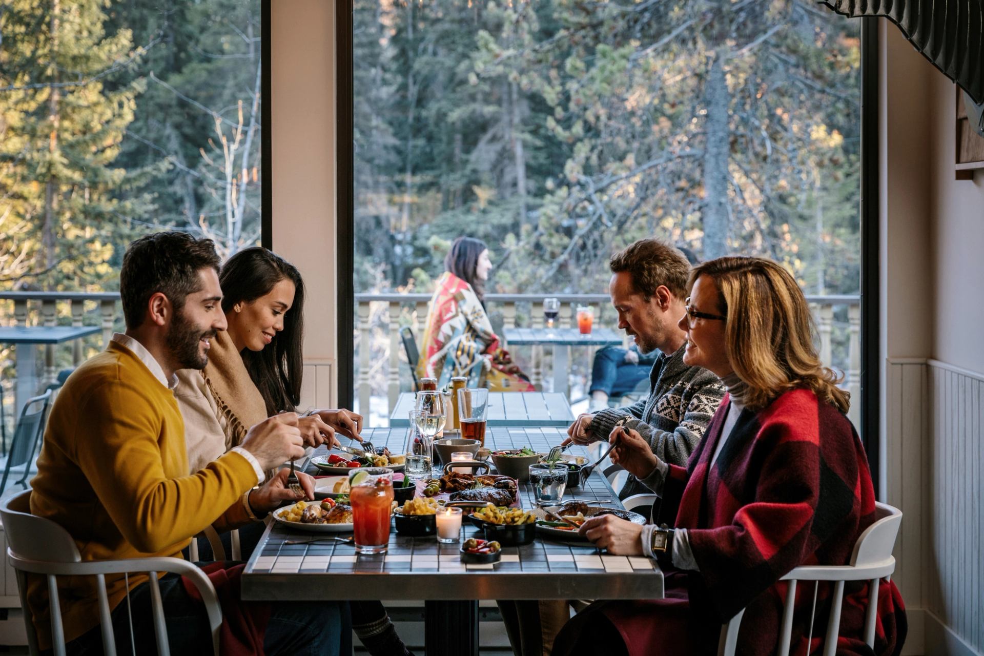 Four friends dining and enjoying a meal with a wooded forest view behind them