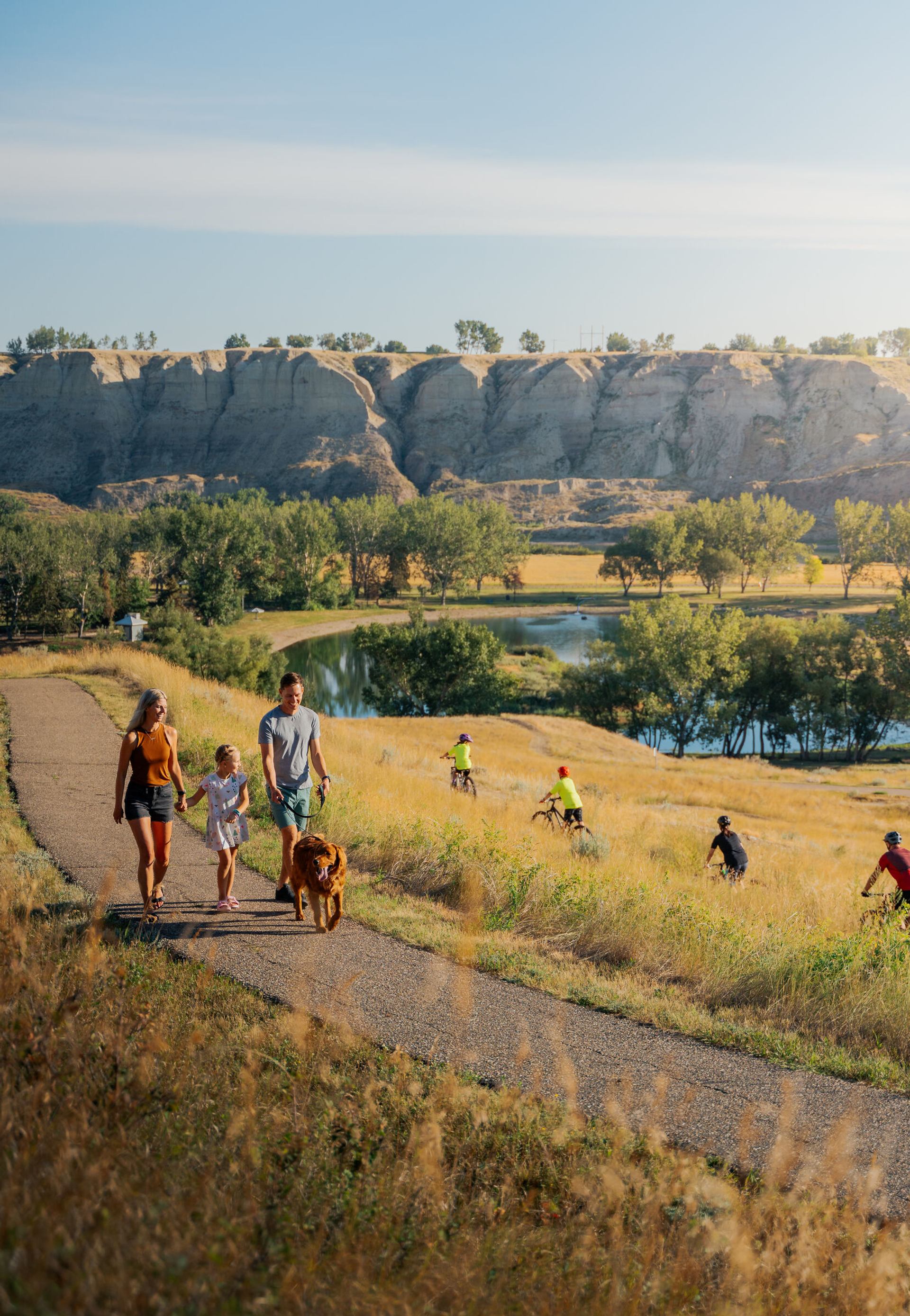 Family walking with a dog while others are mountain biking in Echo Dale Park in Medicine Hat.