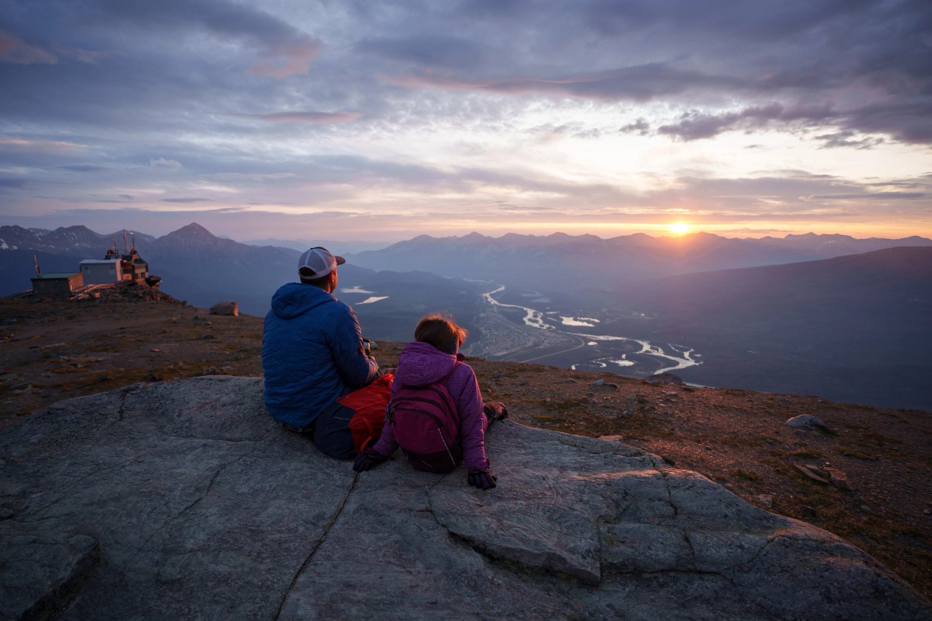 A dad and child sit on a rock and watch the sunset.