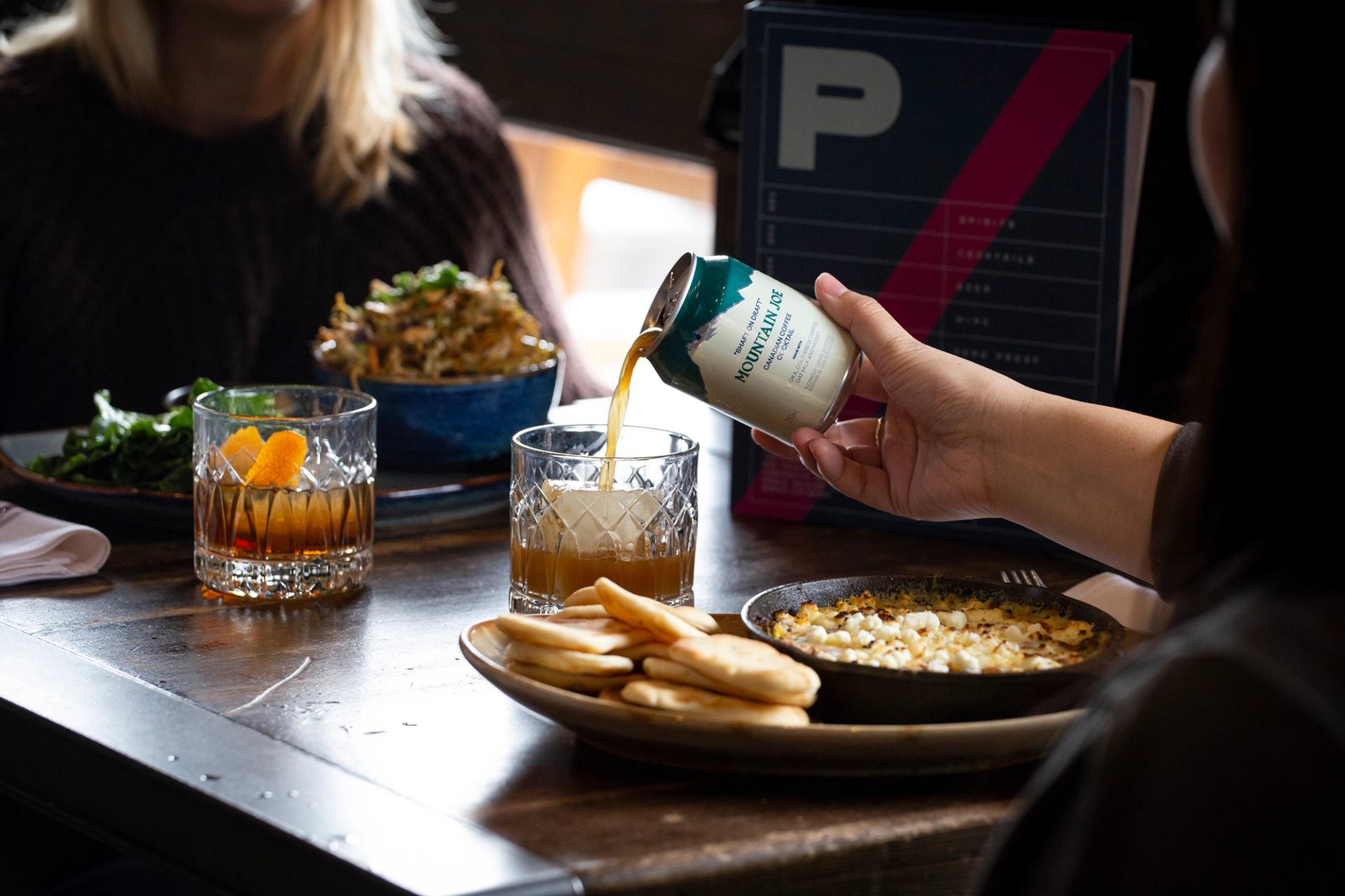 A diner pours a short can of Mountain Joe, a coffee and vodka cocktail, into her glass during dinner at PARK Distillery.
