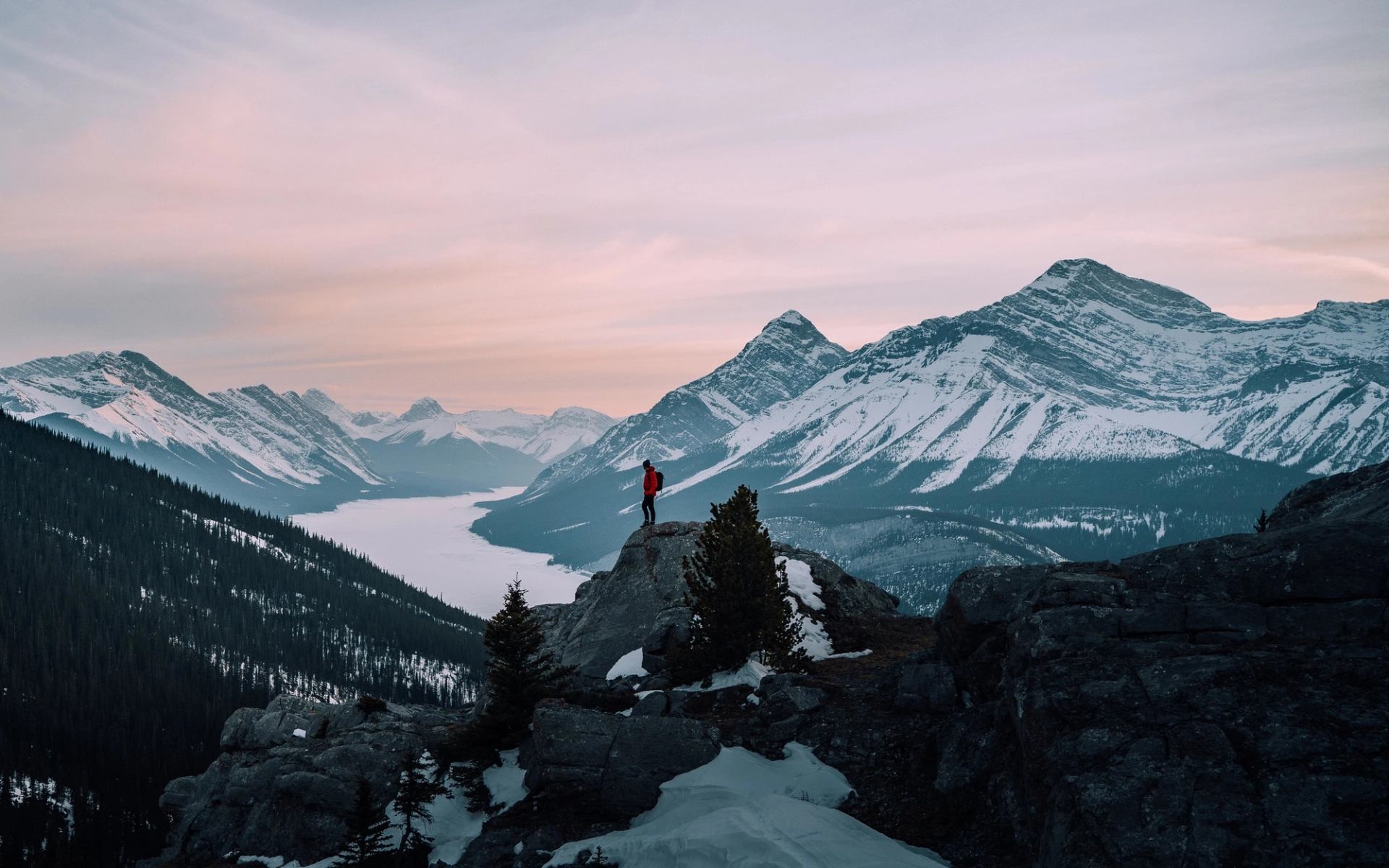 A man stands on the summit of a mountain overlooking the valley and view below.