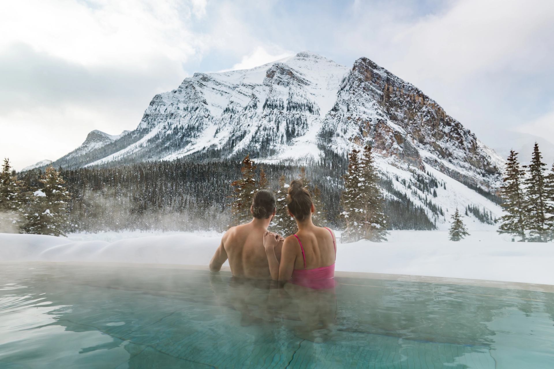 A couple enjoy the view from an outdoor hot tub at BASIN Glacial Waters spa at Fairmont Chateau Lake Louise.