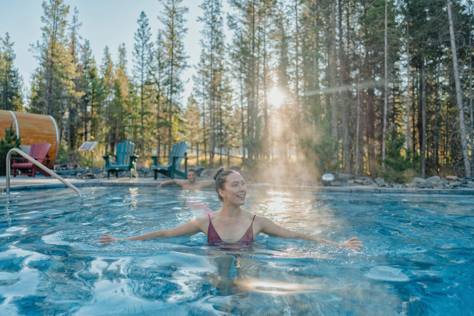 Women standing in pool with sunlight coming through trees and chairs in the background