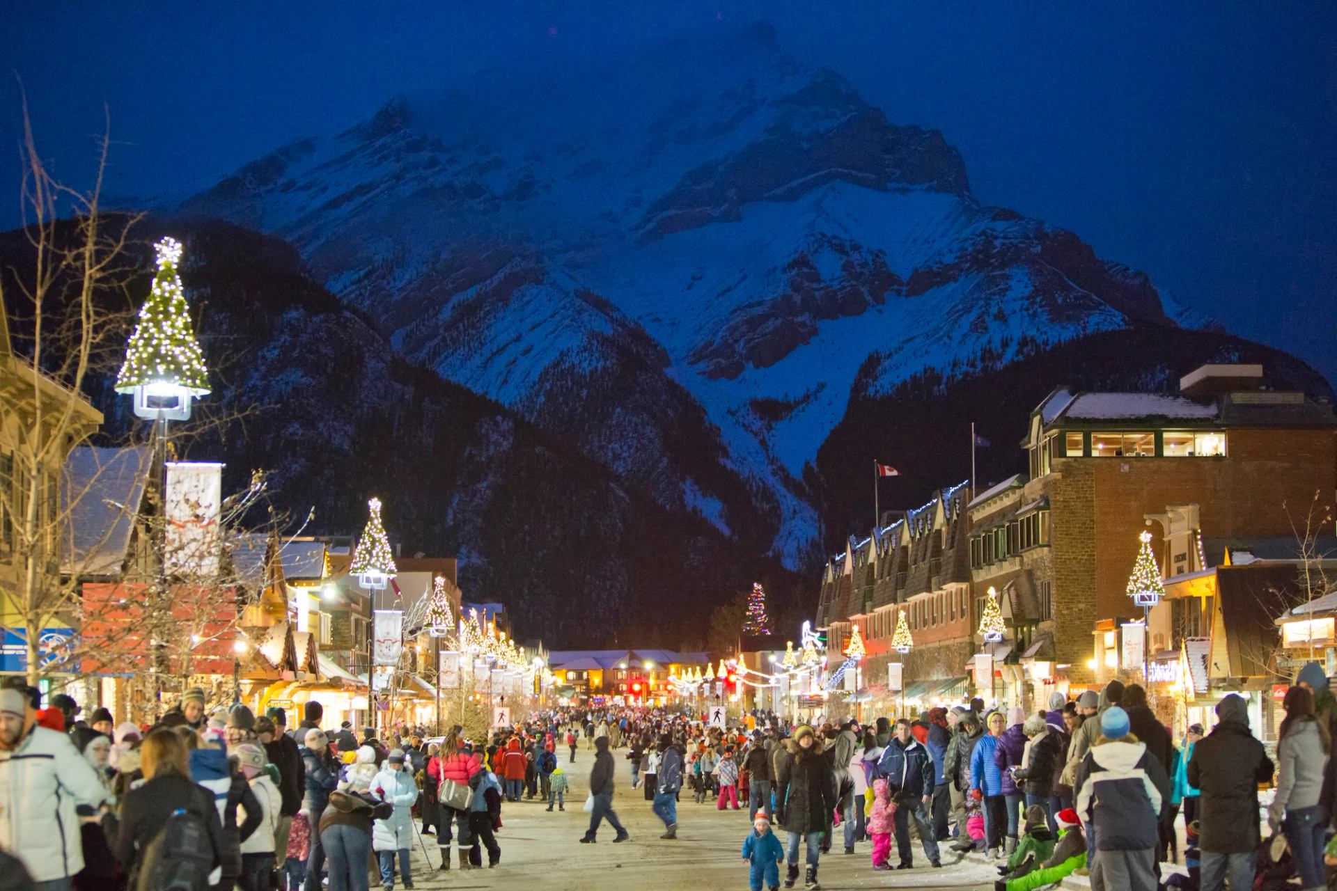 Busy street at night lit by building lights with mountain view lit in the background.