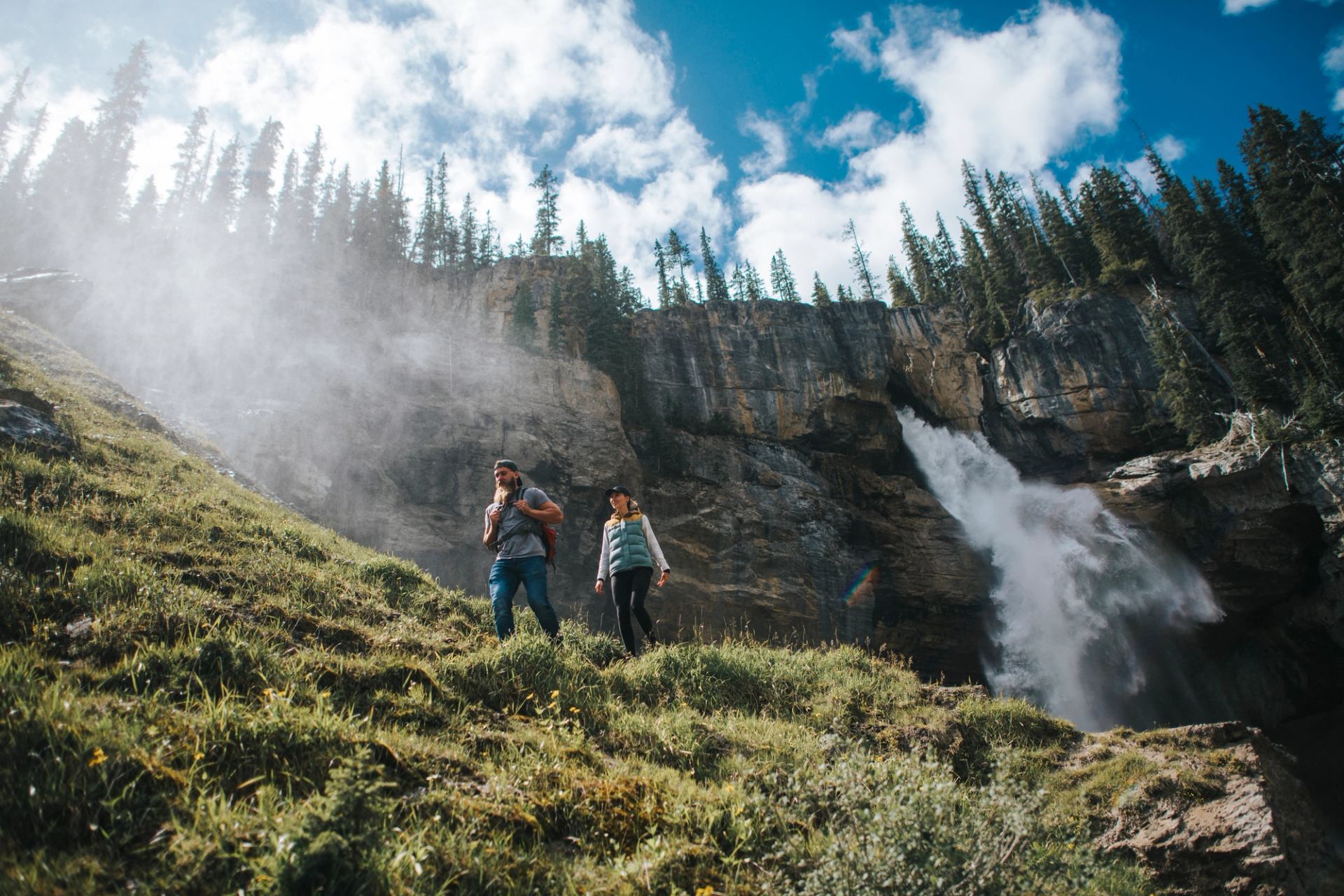Two hikers walk alongside a Panther waterfalls in Banff National Park