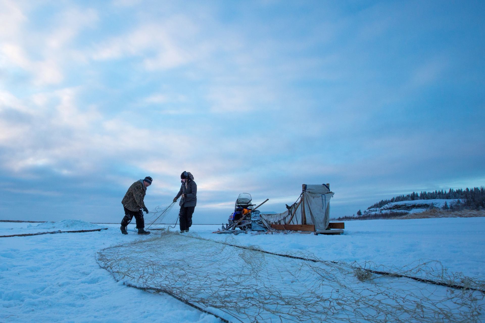 Two people set up their nets and adjust equipment while ice fishing in Fort Chipewyan