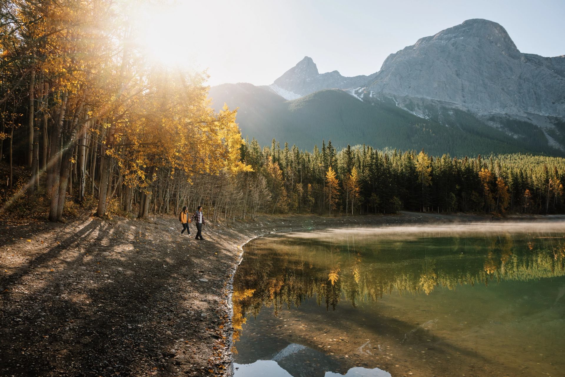 Two people walk on the shore of Wedge Pond in Kananaskis Country.