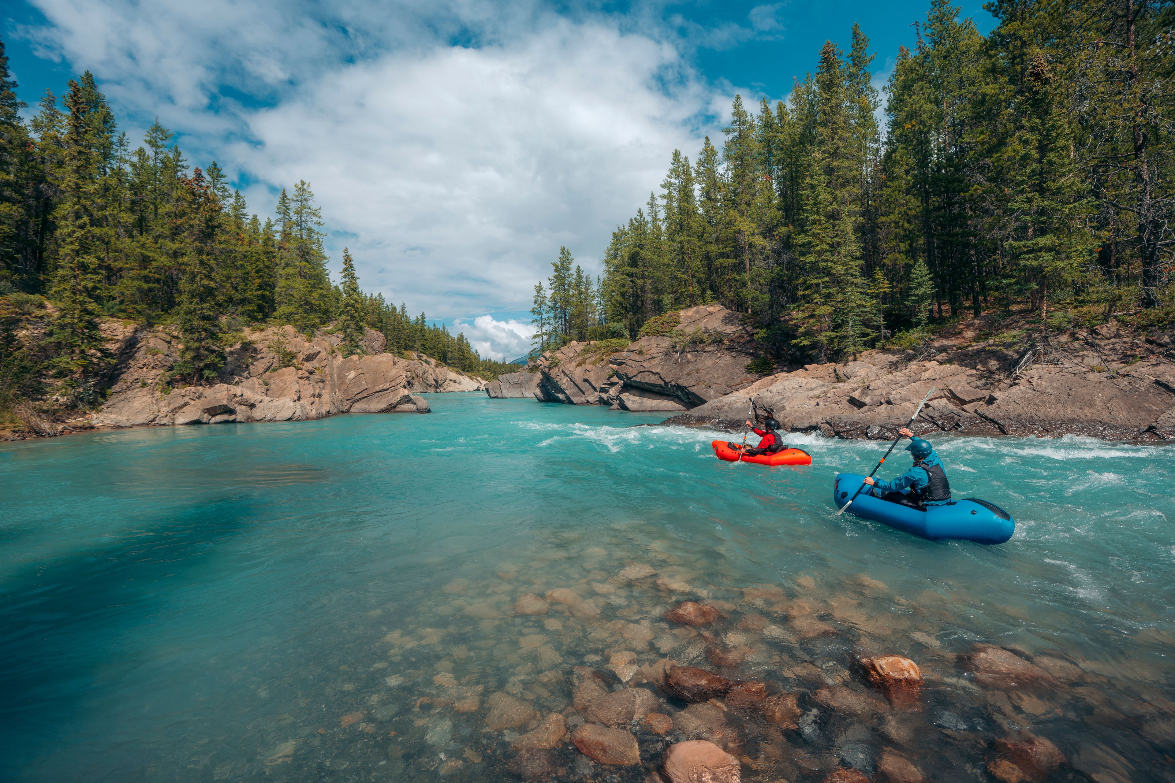 Two pack rafters paddle down the bright blue Cline River in Nordegg.
