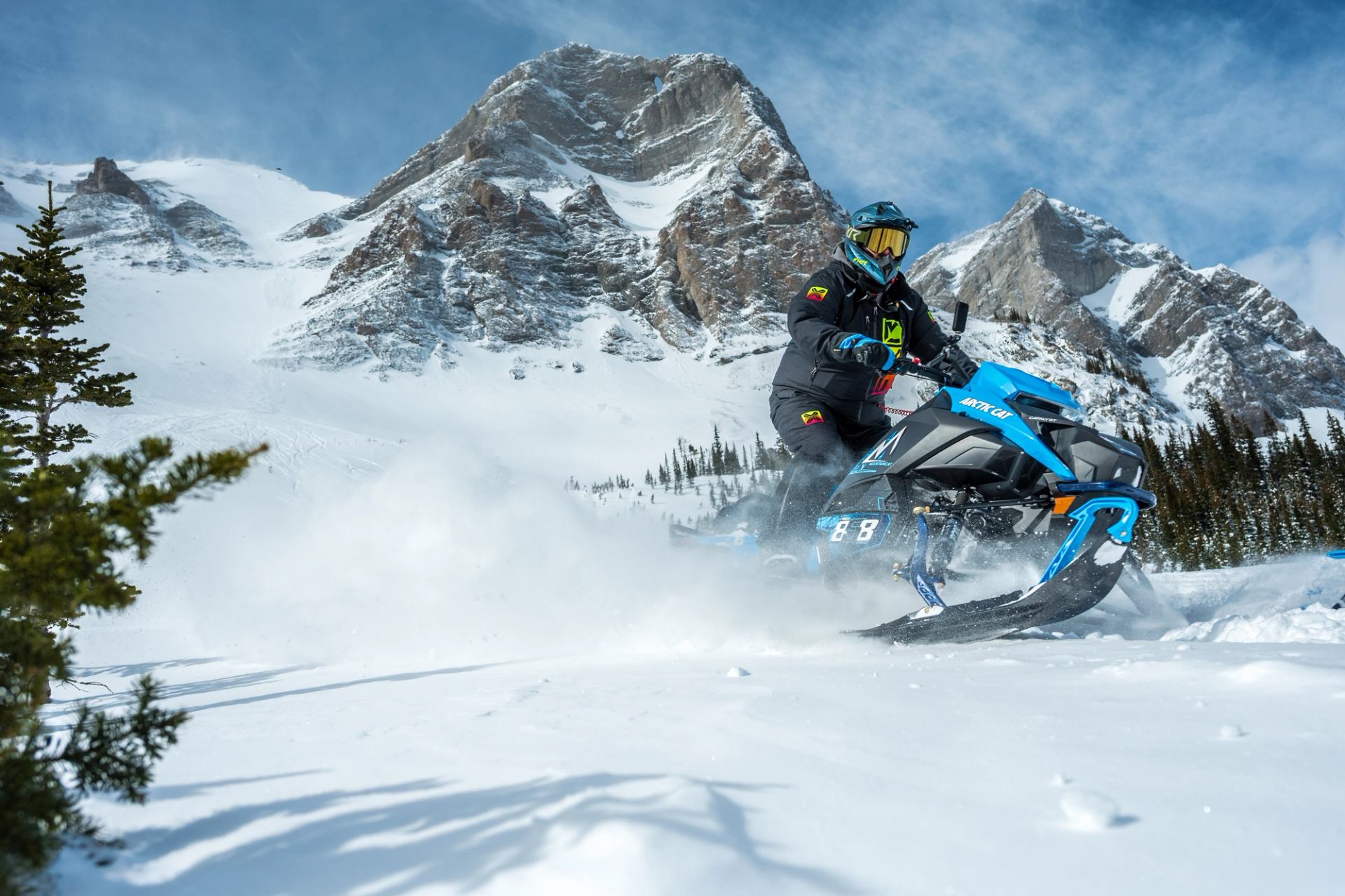 Snowmobiler kicks up powder against a majestic mountain backdrop.