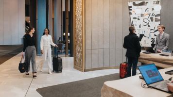 2 women near reception, and another guest and receptionist at JW Marriott Edmonton ICE District.