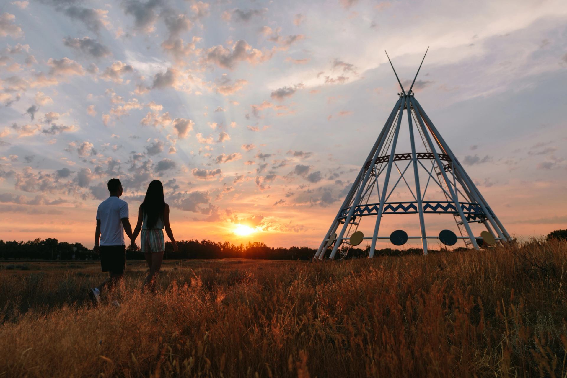 A couple stroll beside the Saamis Tepee at sunset.