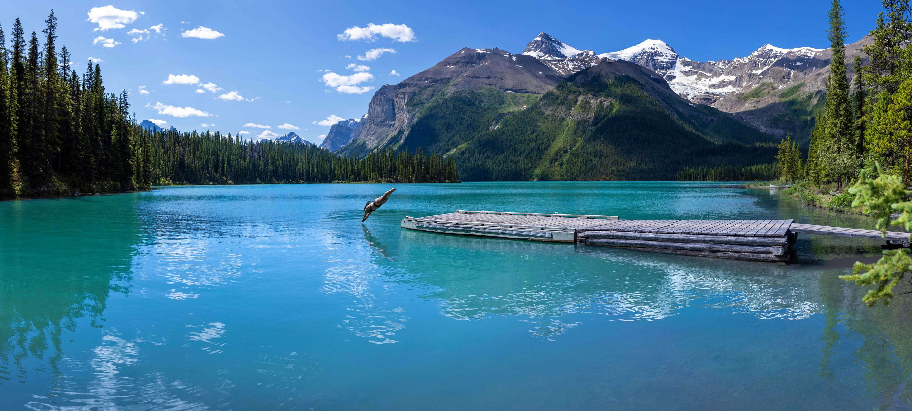 A woman dives off a dock into Fisherman's Bay at Maligne Lake in Jasper National Park.