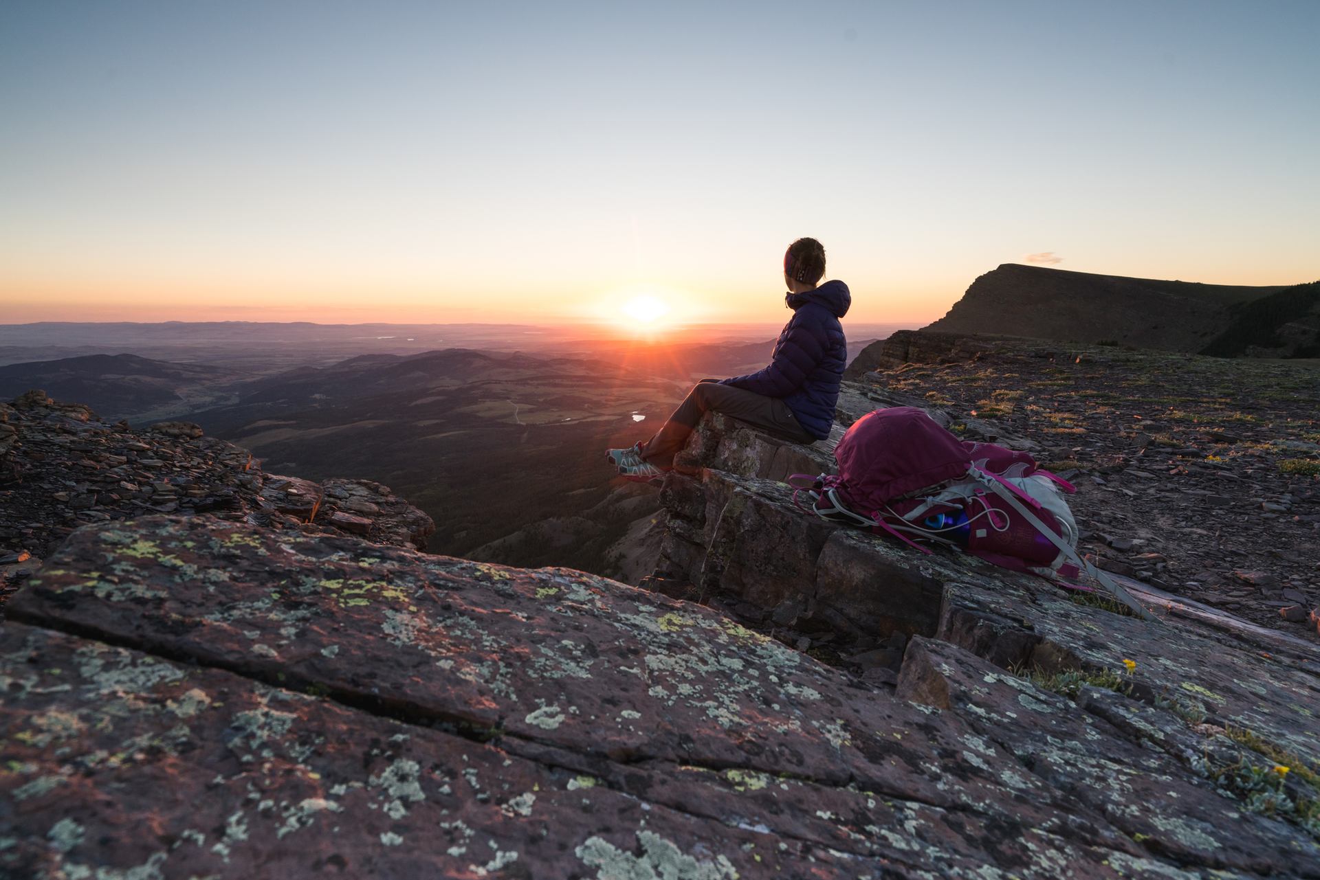 A person sits on a rock, looking out over a valley at sunset.