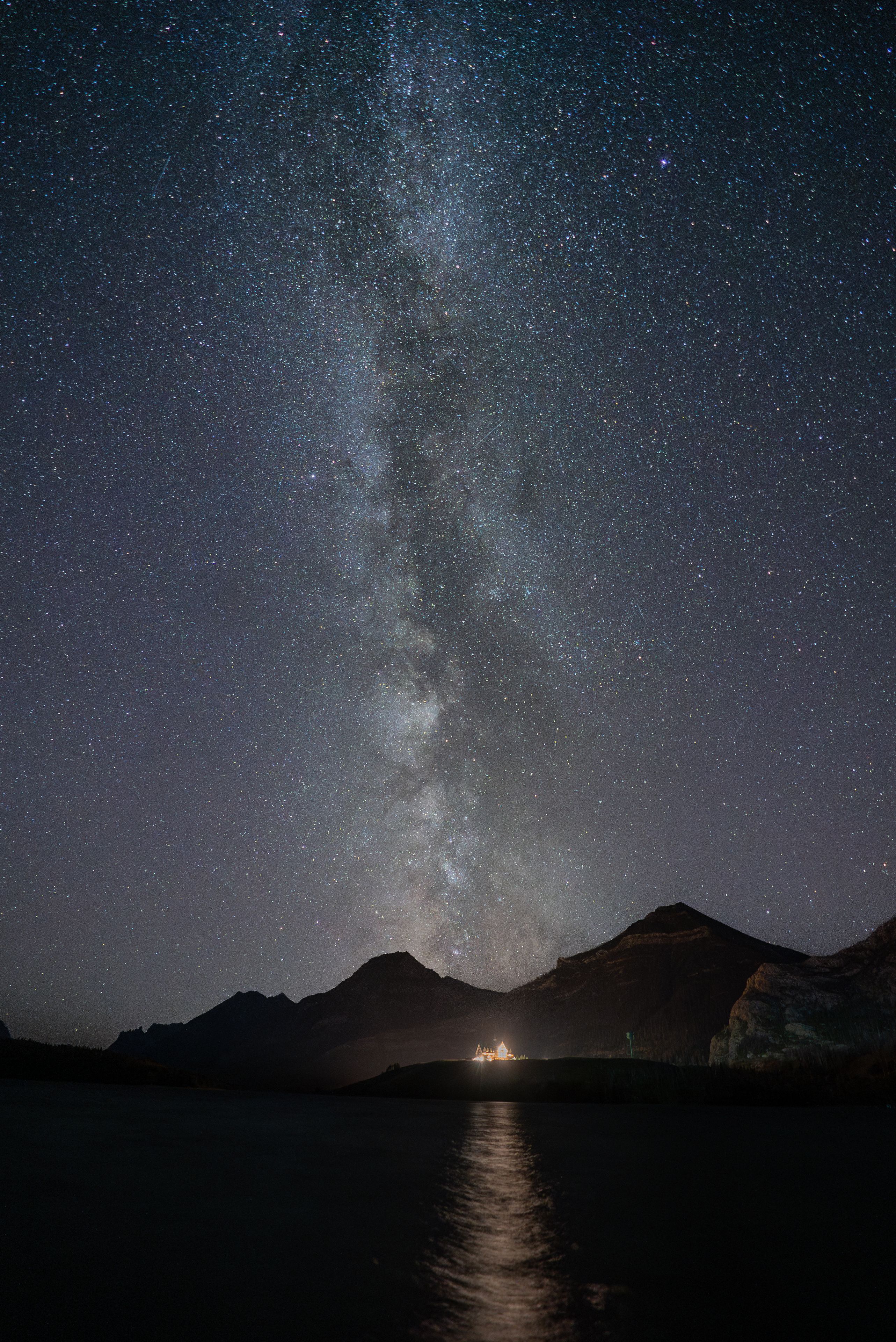 Northern lights above mountains with a starry night sky in Waterton Lake National Park.