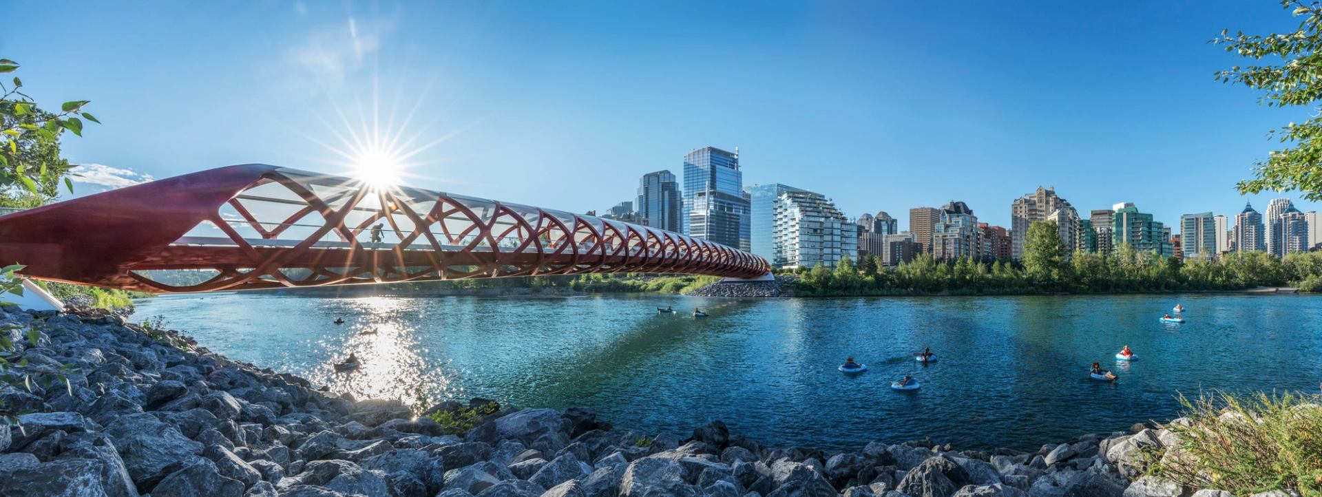 A panoramic view of people floating down a river with the red bridge and cityscape views.