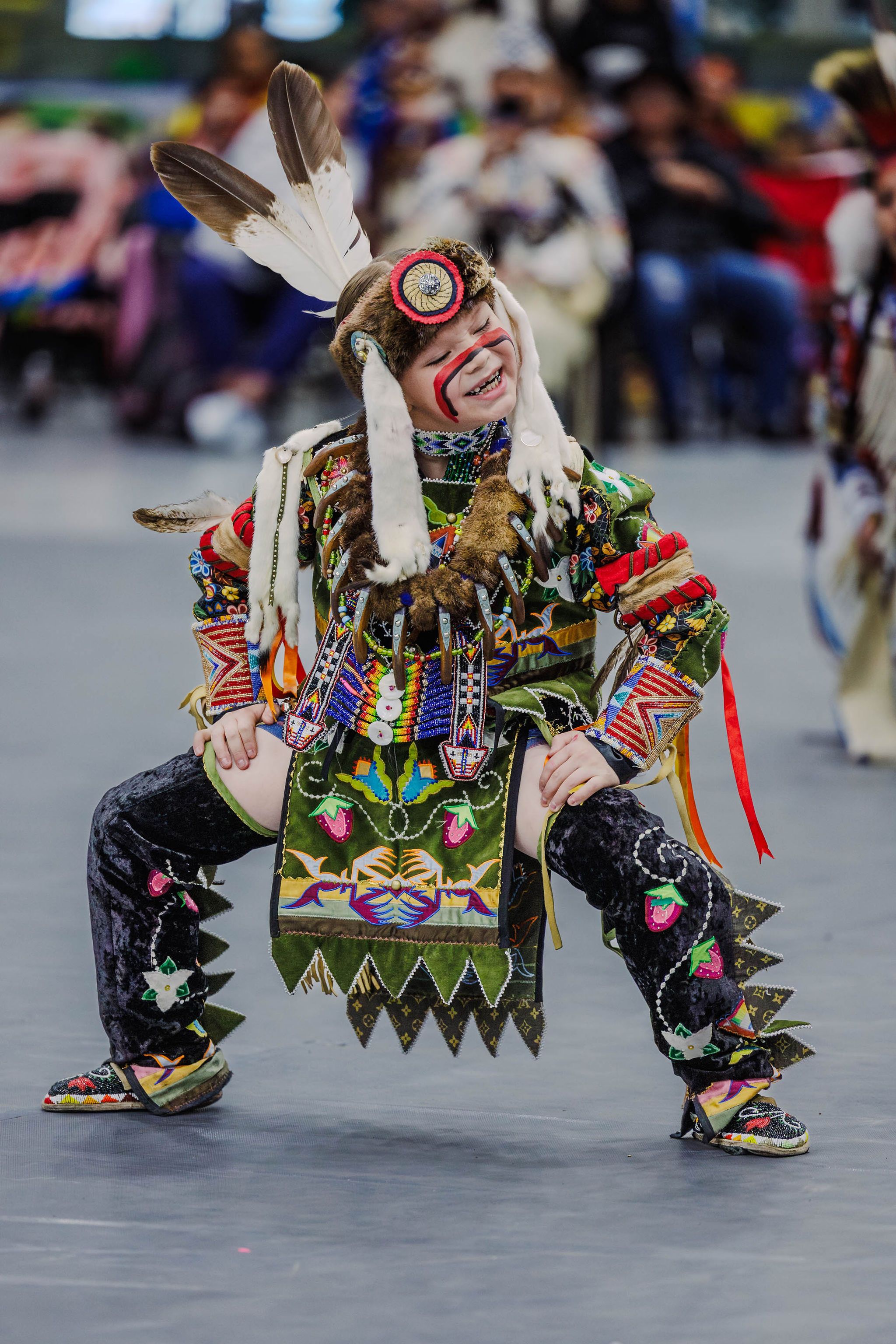 A smiling child in regalia dances at a powwow.