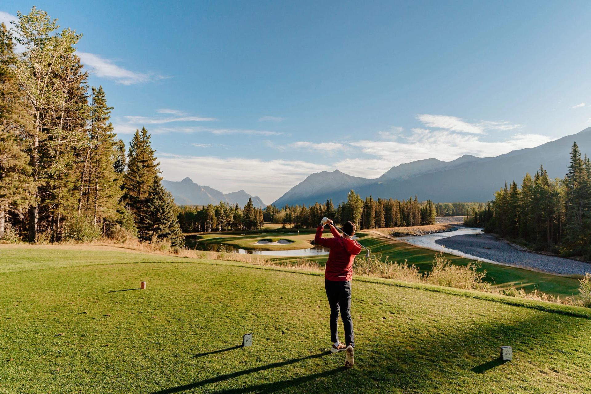 A golfer tees off at the Kananaskis Country Golf Course with mountains in the background.